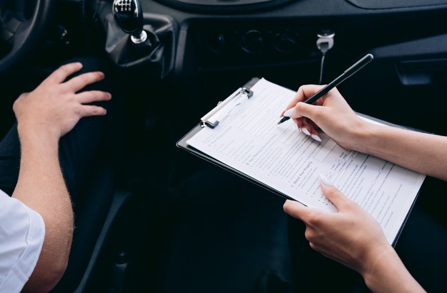 Close-up of a person writing on a clipboard inside a car, showing hands and a gear shift.