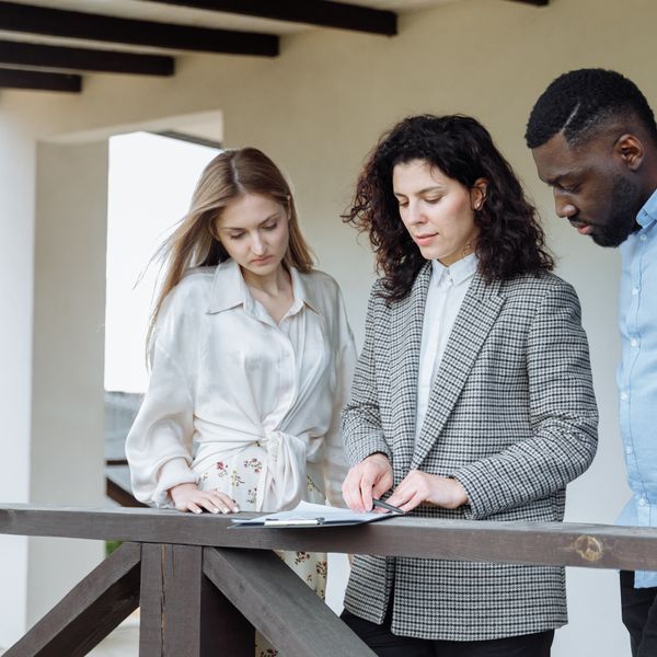 Three adults reviewing documents on a balcony during a real estate consultation.