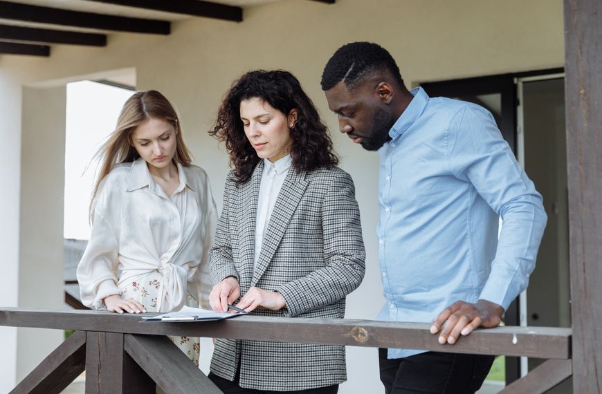 Three adults reviewing documents on a balcony during a real estate consultation.